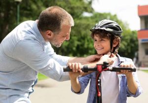 Smiling adult man putting safety helmet on his son